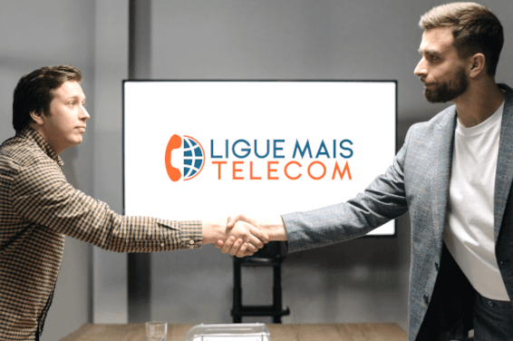 Duas pessoas apertam as mãos em uma reunião, com a marca LigueMais Telecom ao fundo.